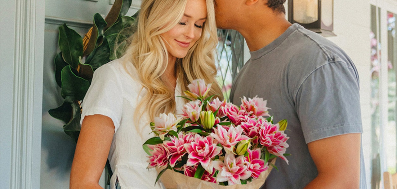 A joyful couple sharing a tender moment, embracing with a bouquet of vibrant pink lilies.