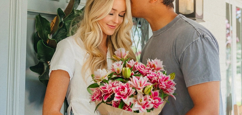 A joyful couple sharing a tender moment, embracing with a bouquet of vibrant pink lilies.