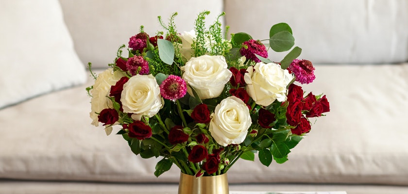 Elegant bouquet of white and red roses with pink accents in a stylish gold vase.