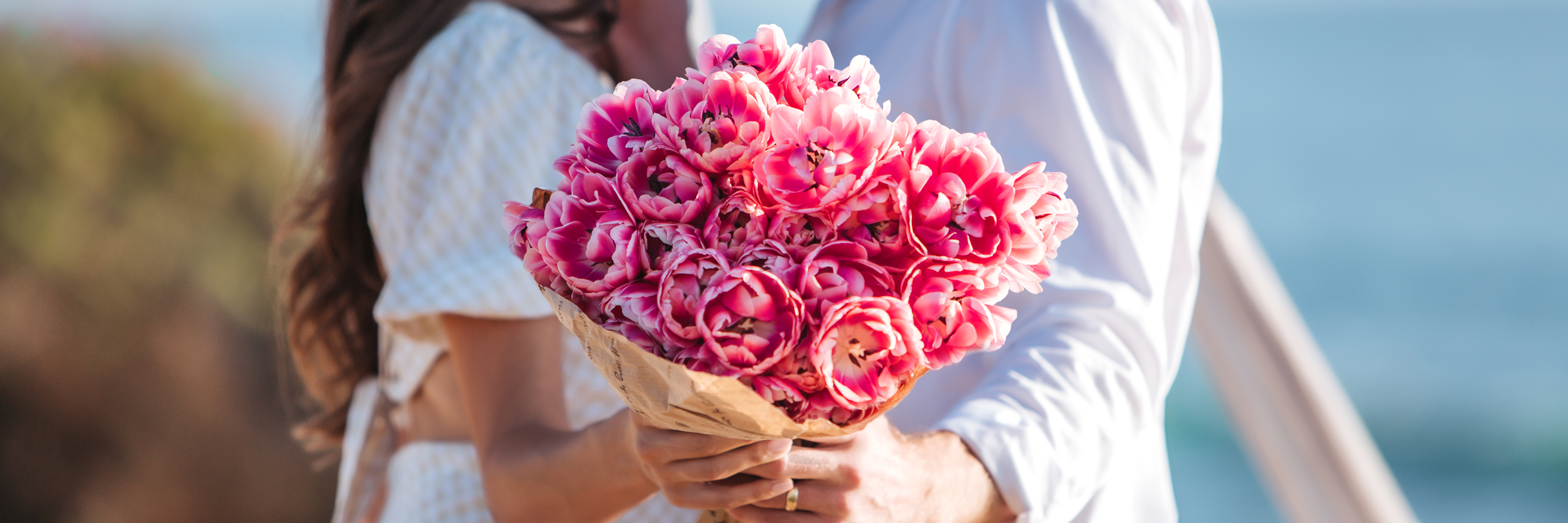 A romantic couple holding a bouquet of vibrant pink tulips by the beach, perfect for any occasion.