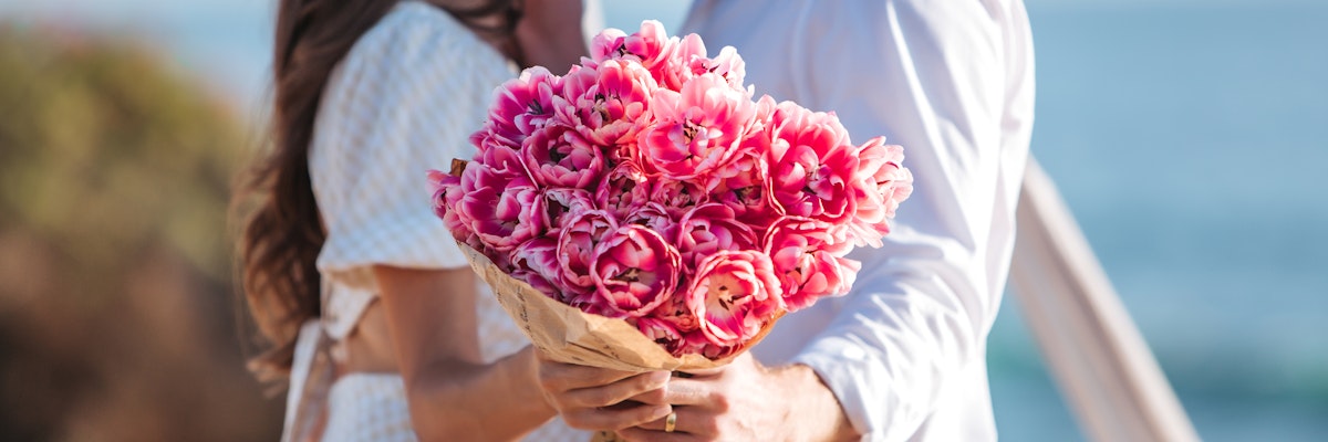 A romantic couple holding a bouquet of vibrant pink tulips by the beach, perfect for any occasion.