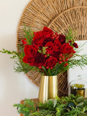 Vibrant red roses and greenery arranged in a stylish gold vase, perfect for home decor.
