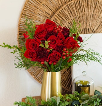 Vibrant red roses and greenery arranged in a stylish gold vase, perfect for home decor.