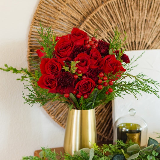 Vibrant red roses and greenery arranged in a stylish gold vase, perfect for home decor.