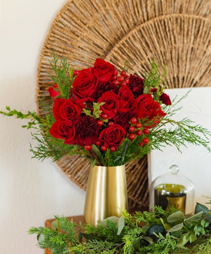 Vibrant red roses and greenery arranged in a stylish gold vase, perfect for home decor.