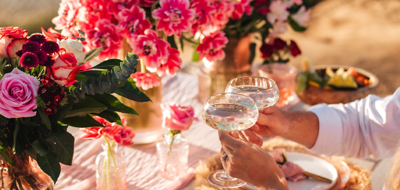 Elegant outdoor table setting with floral centerpieces and sparkling cocktails for a celebration.