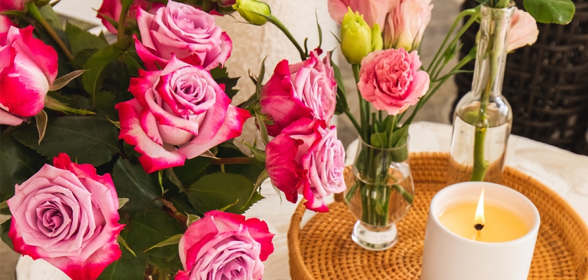 A vibrant arrangement of pink roses and soft blooms paired with a decorative candle.
