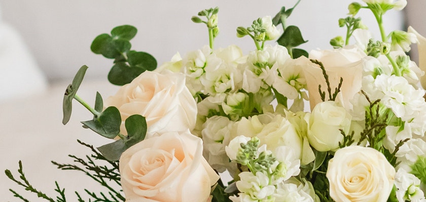 Elegant arrangement of soft peach roses and white blooms with fresh greenery accents.
