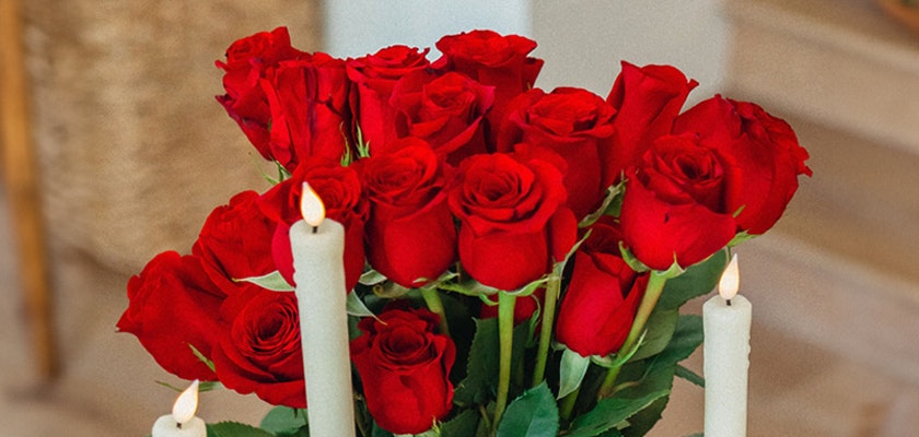 Vibrant bouquet of red roses complemented by elegant white candles, enhancing any romantic setting.