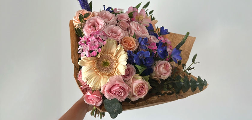 Beautiful mixed bouquet featuring pink roses, blue delphiniums, and a cheerful gerbera daisy.
