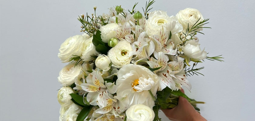 Elegant white floral bouquet featuring ranunculus, lilies, and greenery, perfect for any occasion.