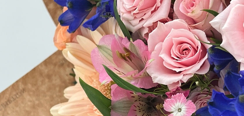 Delicate arrangement of pink roses, blue delphinium, and soft blooms in a charming bouquet.