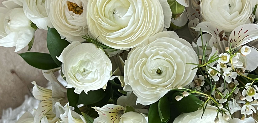 Elegant white floral arrangement featuring ranunculus, delicate blooms, and lush green leaves.