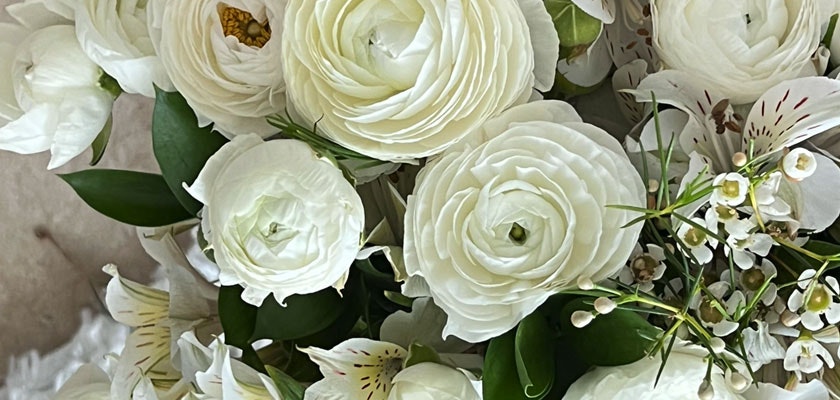 Elegant white floral arrangement featuring ranunculus, delicate blooms, and lush green leaves.
