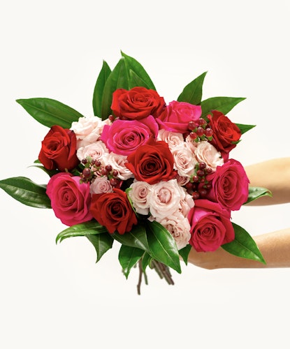 Lush bouquet featuring hot pink and red roses, light pink spray roses, and red hypericum.