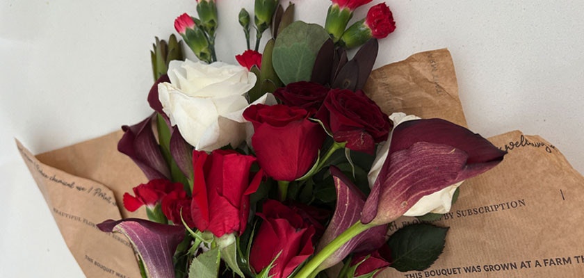 Vibrant bouquet featuring red and white roses, calla lilies, and greenery, elegantly packaged.