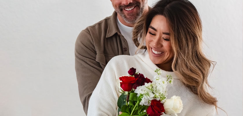 A joyful couple sharing a romantic moment with a beautiful bouquet of roses and white flowers.