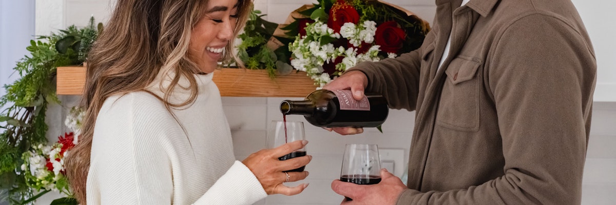 A couple enjoying a cozy wine moment at home, surrounded by festive floral decor.