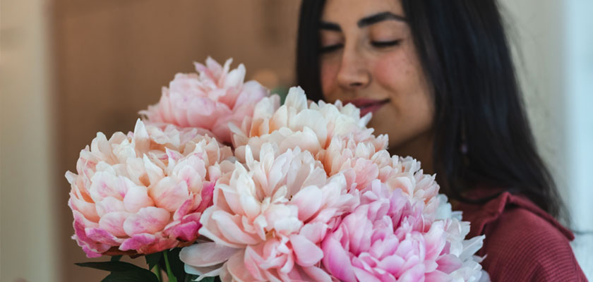 A woman enjoying a stunning bouquet of soft pink peonies, radiating beauty and charm.