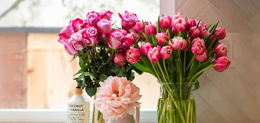 A vibrant display of pink roses and tulips next to a stylish vase, adding elegance to any setting.