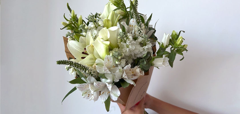 Elegant white floral bouquet featuring lilies, alstroemeria, and greenery in natural packaging.