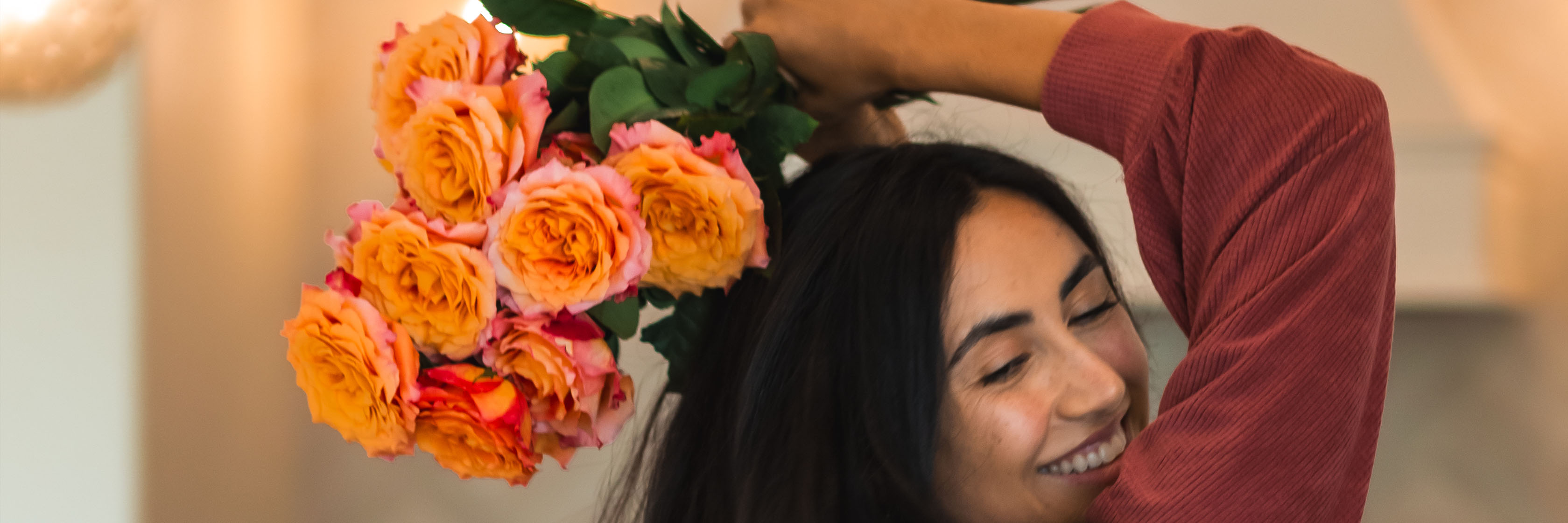 A joyful woman holds a vibrant bouquet of orange and pink roses, celebrating love and happiness.