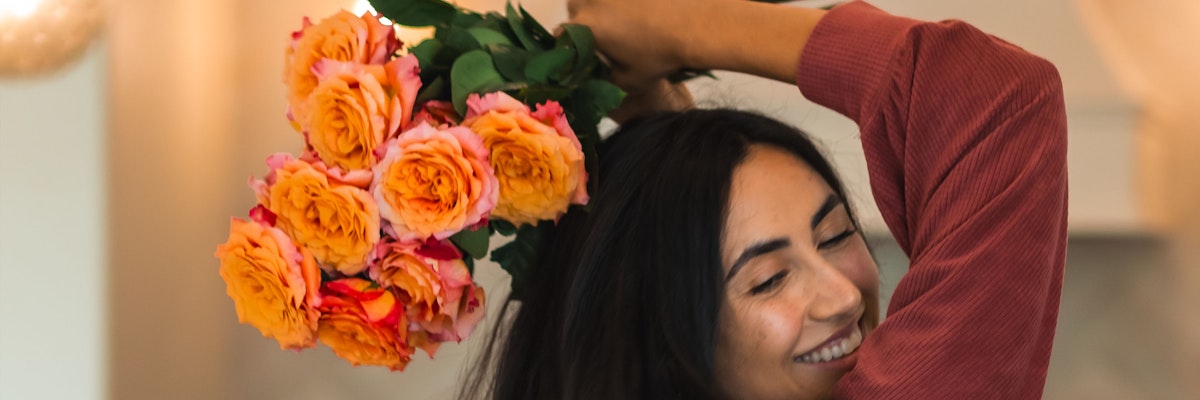 A joyful woman holds a vibrant bouquet of orange and pink roses, celebrating love and happiness.