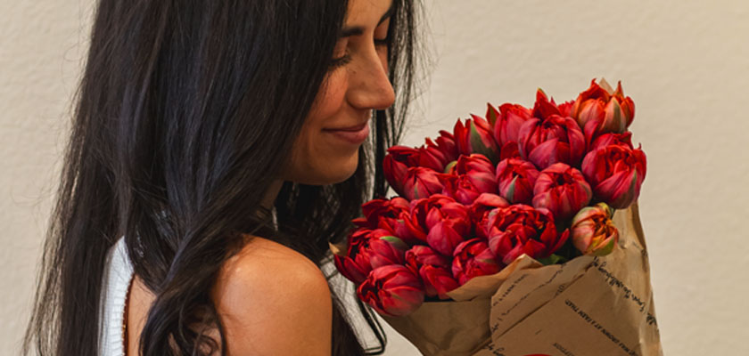 A woman joyfully holding a vibrant bouquet of red tulips wrapped in elegant paper.