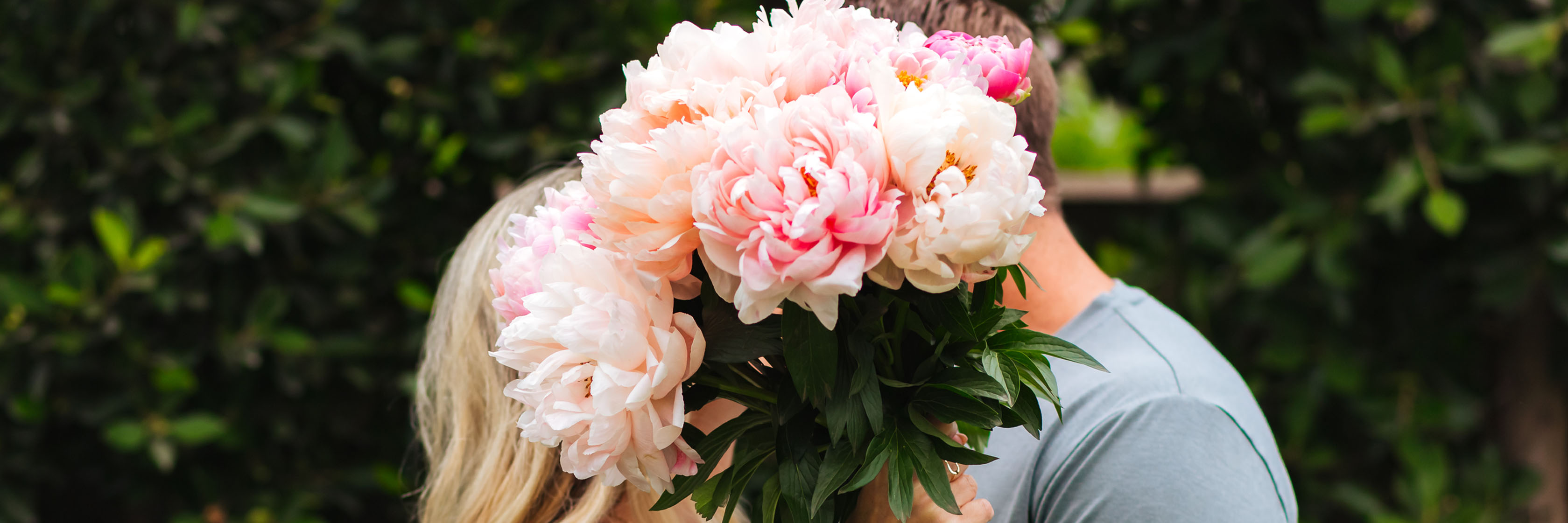 A lush bouquet of pink peonies held by a couple, symbolizing love and connection amidst greenery.