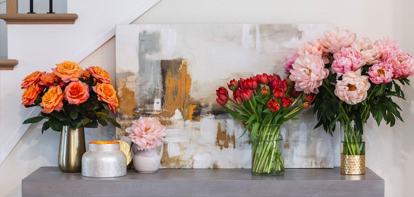 A vibrant floral display featuring orange roses, red tulips, and pink peonies in stylish vases.