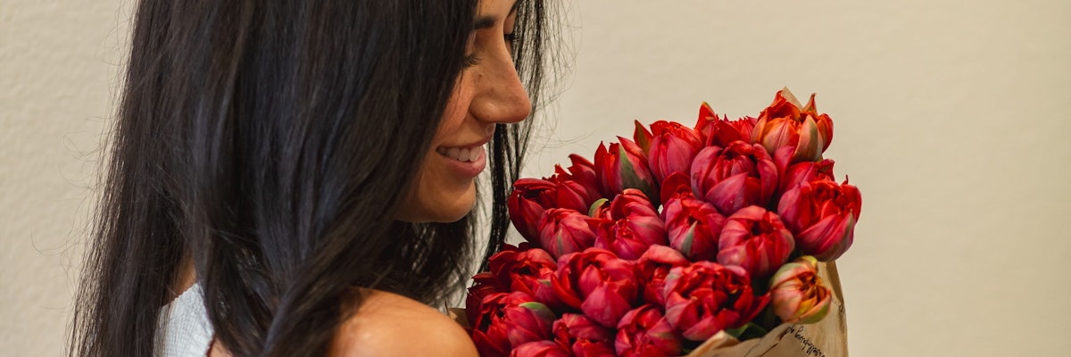 Woman smiling while holding a vibrant bouquet of red tulips, highlighting elegance and joy.