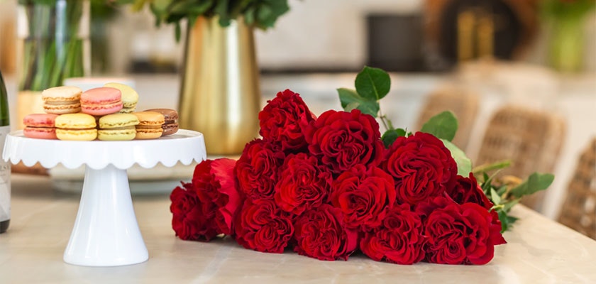 Vibrant red roses elegantly arranged next to a display of colorful macarons.