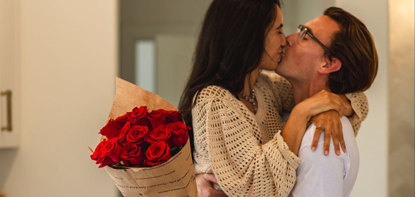 Couple sharing a loving moment with a bouquet of red roses, celebrating romance.