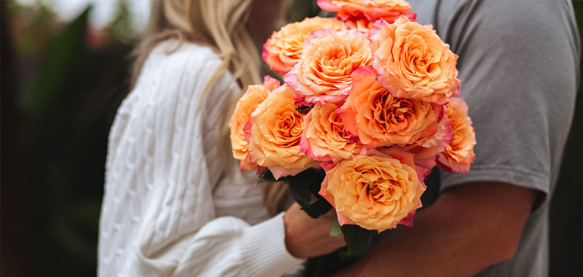 Lush bouquet of vibrant coral roses held by a couple, symbolizing love and affection.