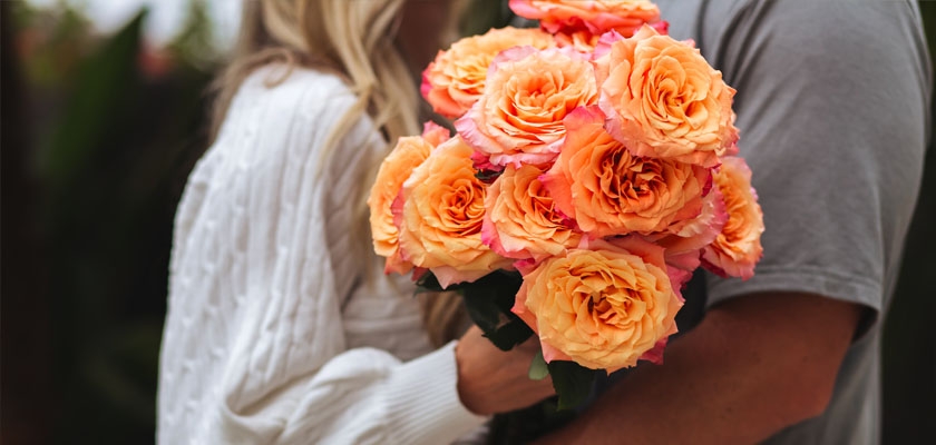 Lush bouquet of vibrant coral roses held by a couple, symbolizing love and affection.