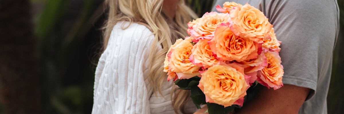Lush bouquet of vibrant peach roses held by a couple, symbolizing love and romance in nature.