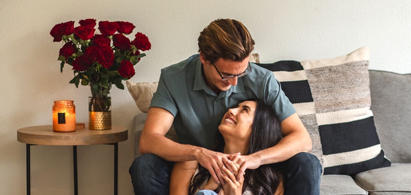 A loving couple sharing a joyful moment at home, surrounded by red roses and cozy decor.