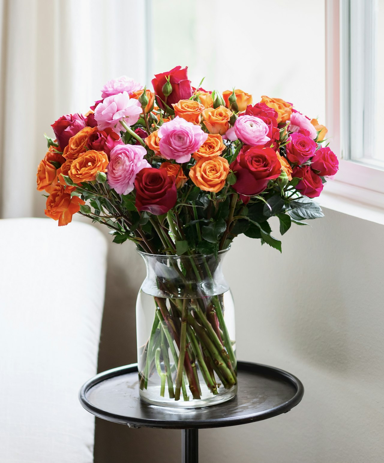 Freshly arranged bouquet of orange, pink, and red roses in a glass vase on a side table.