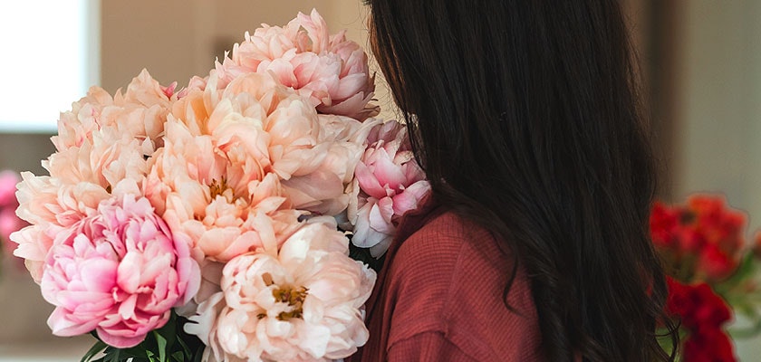 A woman cradles a lush bouquet of soft pink peonies, exuding elegance and charm.