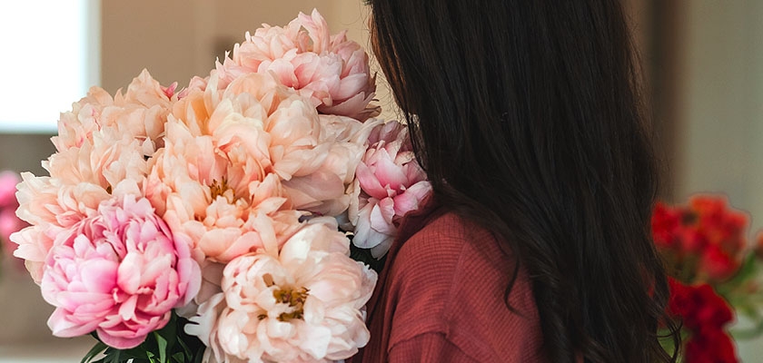 A woman cradles a lush bouquet of soft pink peonies, exuding elegance and charm.