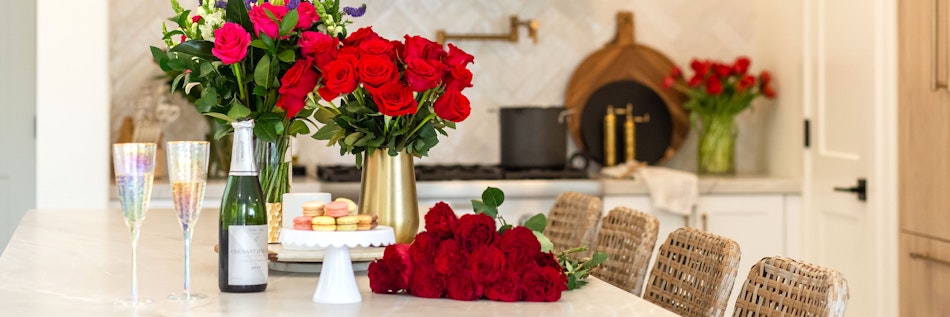 Elegant kitchen setting featuring vibrant red roses, champagne, and delightful pastries.