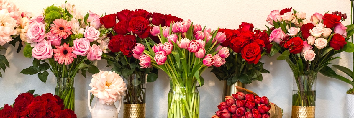 Vibrant floral display featuring red roses, pink tulips, and assorted blooms in elegant vases.
