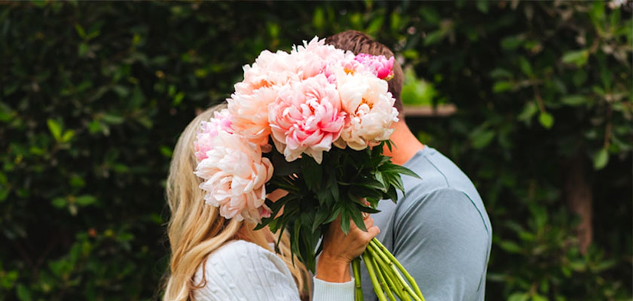 A lush bouquet of pastel peonies held by a couple, symbolizing love and romance in a garden setting.