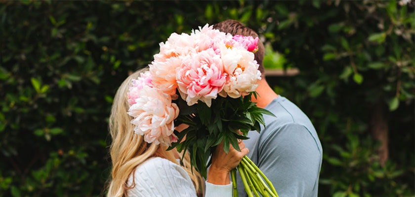 A lush bouquet of pastel peonies held by a couple, symbolizing love and romance in a garden setting.