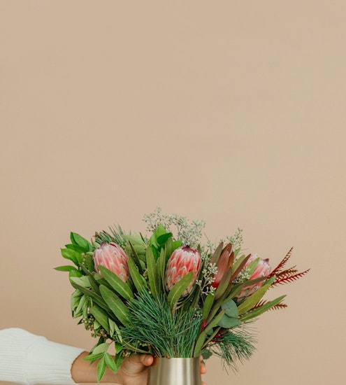A stunning bouquet featuring protea, greenery, and accents in a stylish vase, perfect for decor.