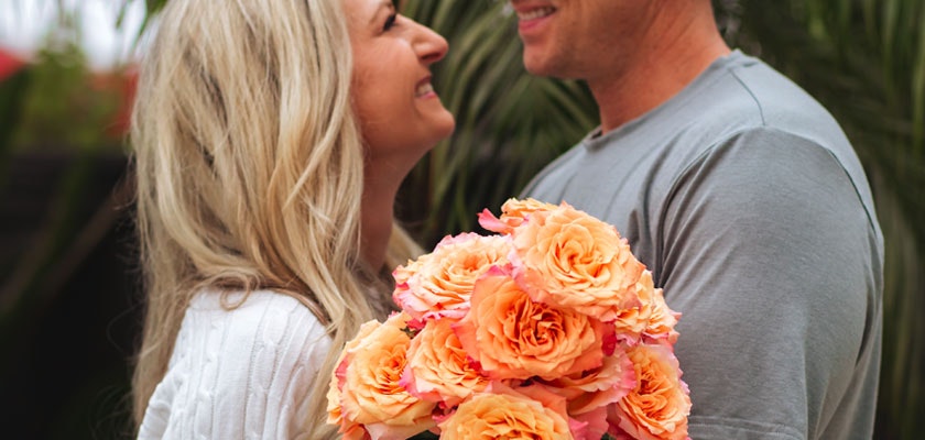 A couple joyfully sharing a moment, holding a vibrant bouquet of peach roses in a romantic setting.