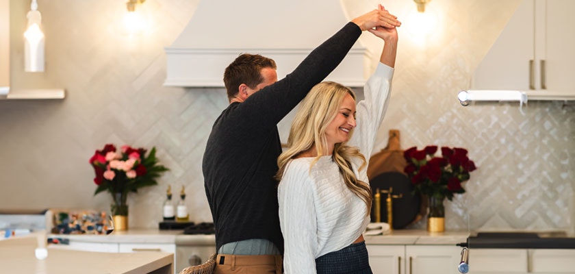 A joyful couple dancing in a modern kitchen filled with vibrant flowers and warm lighting.