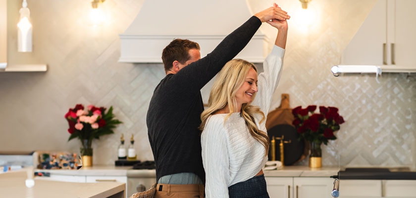 A joyful couple dancing in a modern kitchen filled with vibrant flowers and warm lighting.