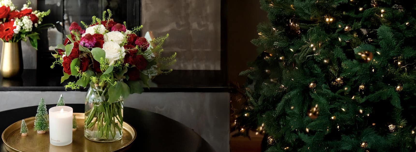 Festive floral arrangement featuring red and white blooms beside a decorated Christmas tree.