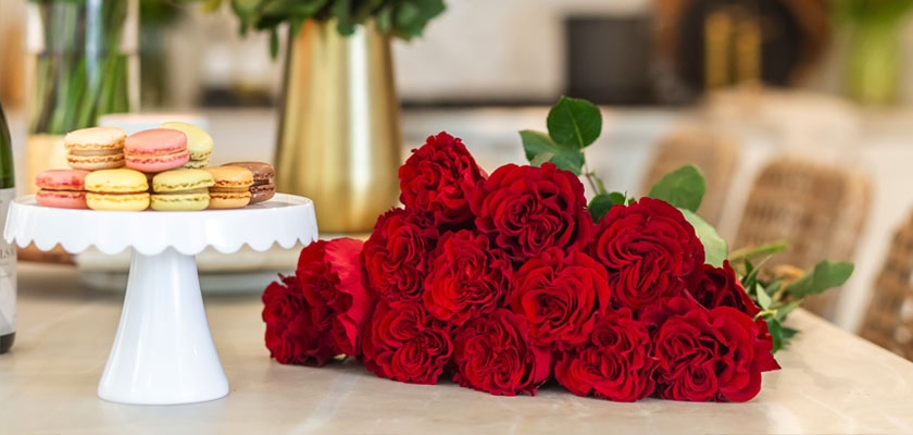 Lush bouquet of red roses beside a decorative plate of colorful macarons, ideal for celebrations.